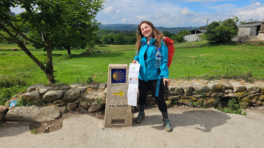 Elisa ao lado de um marco do Caminho, em meio a um campo verde